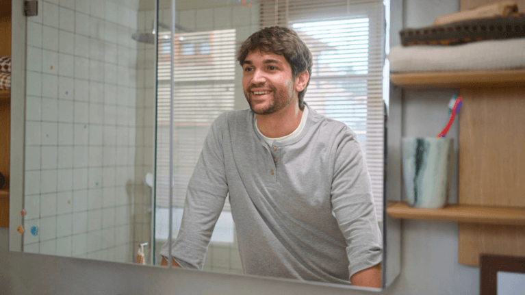 A young man looks into the bathroom mirror and smiles.