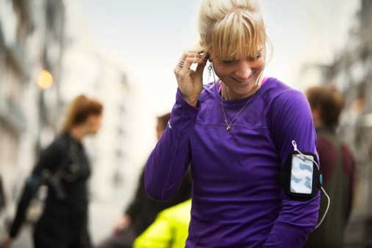 group of runners preparing in urban invironment, young female athlete plugging in her earphones 