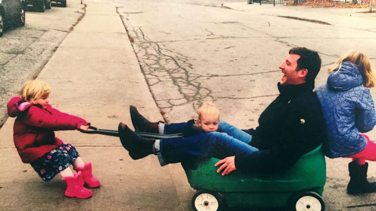 Photo of Janine Cole's husband being pulled in a toy wagon by their children. husband came out as gay