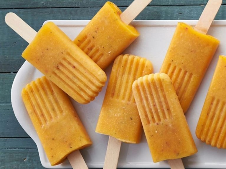 A white tray of Peach ice pops on wooden popsicle sticks with a blue-green wooden background