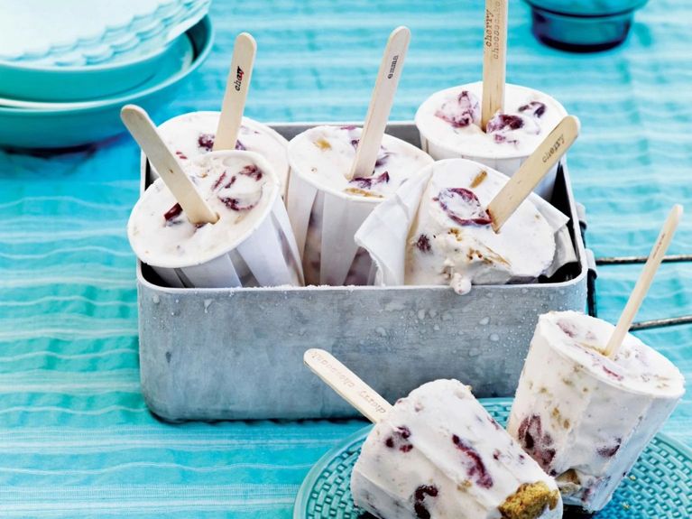 Cherry cheesecake ice cream ice pops formed in Dixie cups with popsicle sticks in a pan after being frozen; the ice pops are made with coarsely chopped graham-crackers; cream; cream cheese; honey; lime juice; cherries for a post on a cherry cheesecake ice cream ice pop recipe