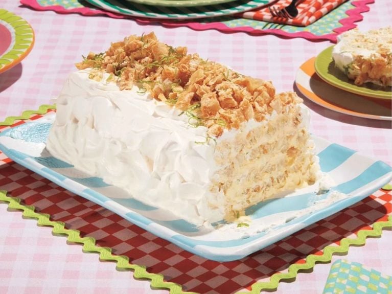 A rectangular cake made with layers of mango and lime cream, strips of puff pastry, frosted with whipped cream and tipped with crunchy toasted coconut flakes.