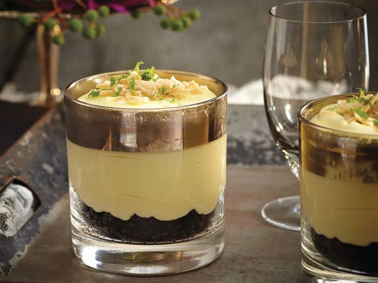 Margarita puddings, made with lime juice, tequila and triple sec, in a glass served over an Oreo cookie crumb crust and topped with tequila cream and toasted coconut and lime zest for a post on an easy margarita pudding recipe for entertaining