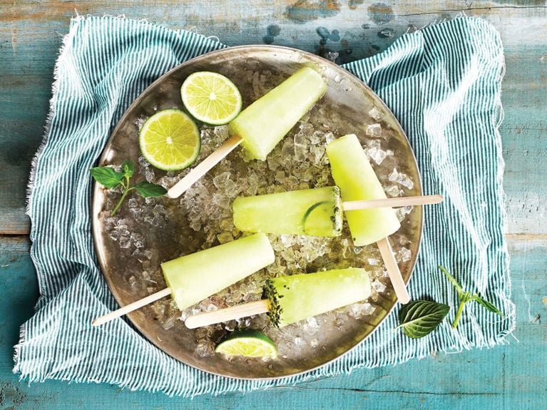 A serving platter covered with ice and mojito ice pops which are green with slices of lime and fresh basil on a striped napkin
