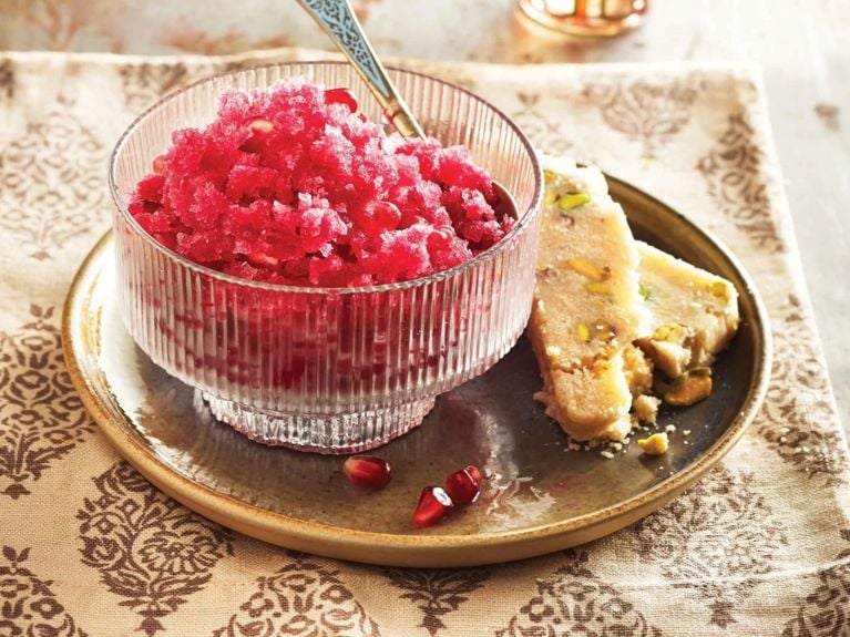 a pomegranate granita in a bowl with a spoon; the granita is made of pomegranate juice; lemon juice; orange flower water and garnished with pomegranate seeds for a post on a cooling pomegranate granita recipe