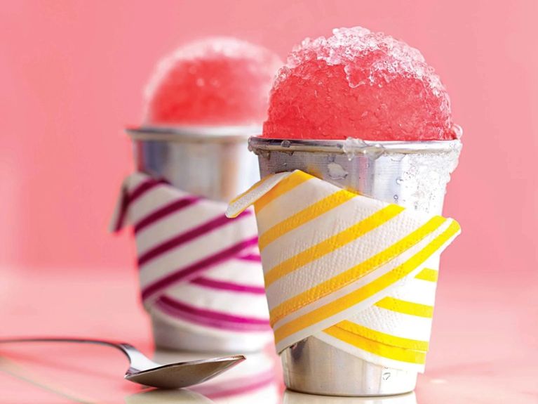 Rhubarb snow cones made with rhubarb syrup in a metal cup with colourful napkin wrappings for a post on an easy summer rhubarb snow cone recipe