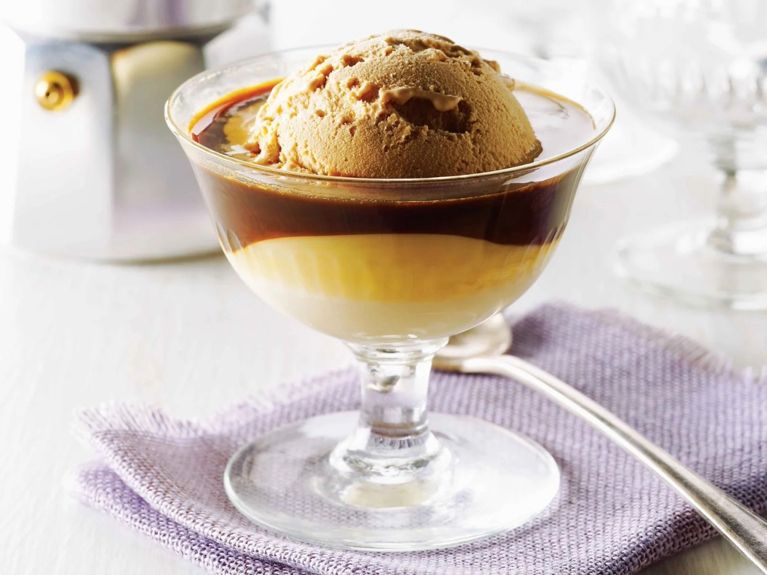 Vietnamese espresso affogato in a glass coupe bowl next to an espresso maker. The affogatto is made with coffee ice cream; sweetened condensed milk and hot espresso for a post on an easy Vietnamese espresso affogatto recipe
