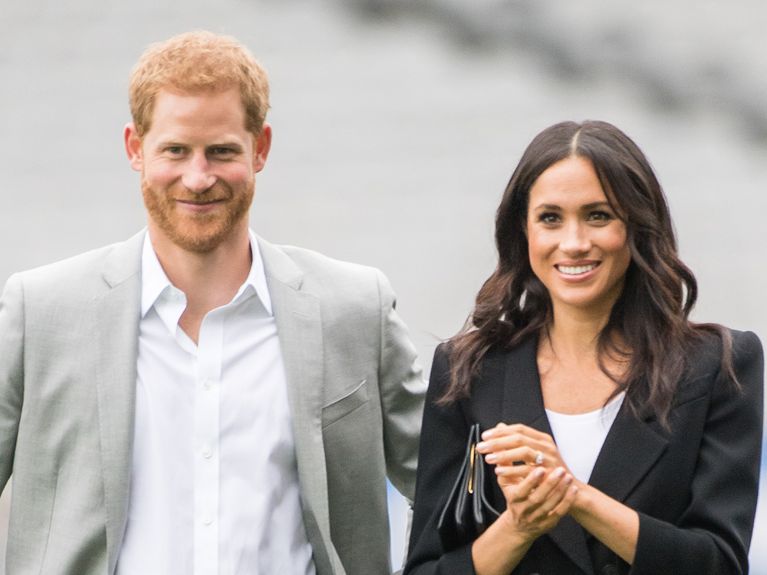Prince Harry and Meghan Markle adopt a labrador dog: here they stand together with Harry in a white shirt and grey suit jacket, Meghan in a black suit jacket