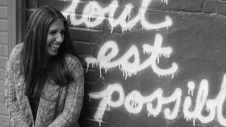 A woman smiles by a graffiti wall for a piece titled "I Lost My Child When I Was 20 Weeks Pregnant, But I’m Still Her Mother"