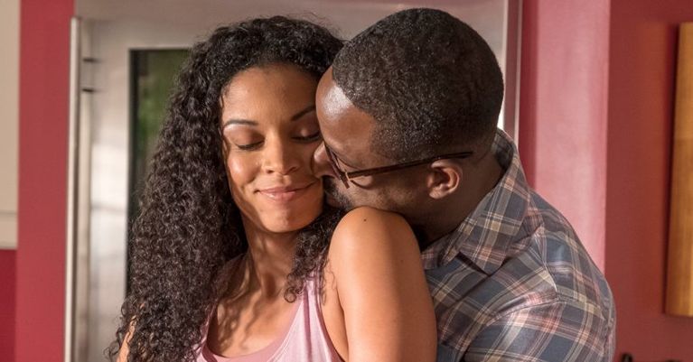 A man hugs a woman from the side and kisses her cheek as she smiles