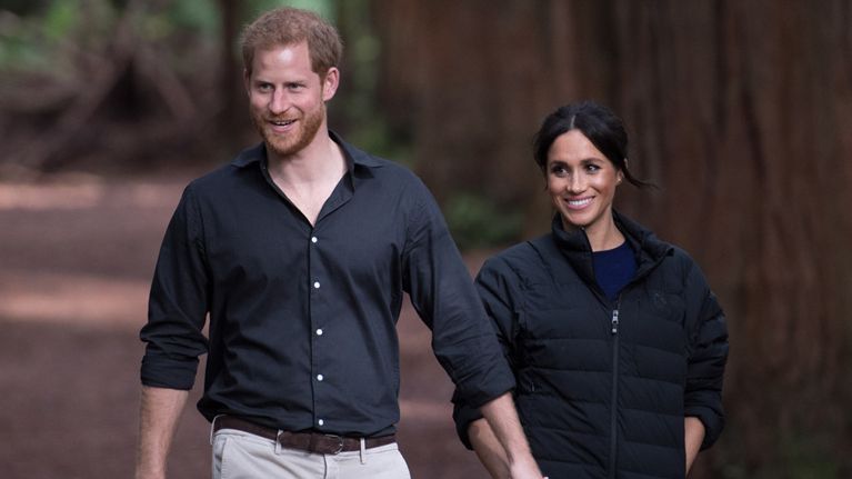 Prince Harry and Meghan Markle walking down a path holding hands and smiling.