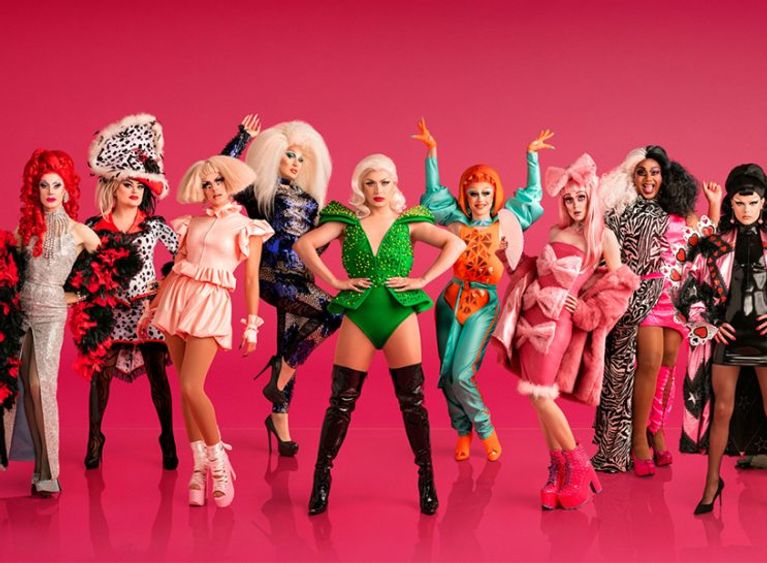 A group of people dressed in costume drag pose against a hot pink background