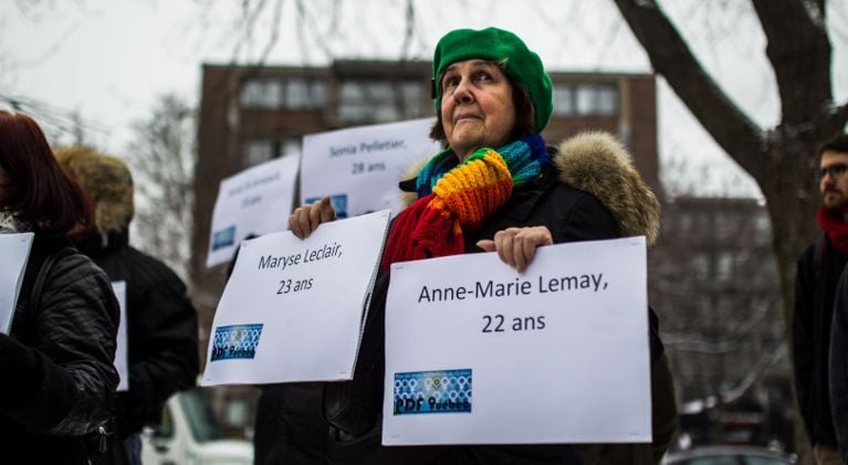 Woman holding a sign that bears the victim's names at vigil.