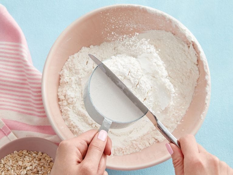 levelling a scoop of flour with a knife to show how to measure flour for easy, healthy oat whole wheat buttermilk pancakes recipe