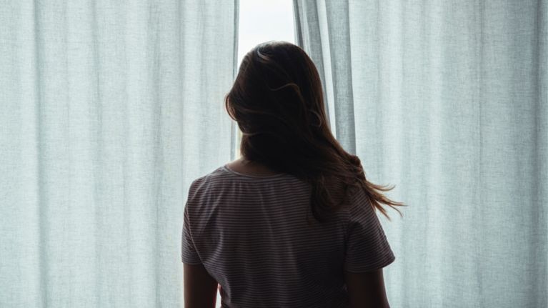 A woman looks out a window between two curtains