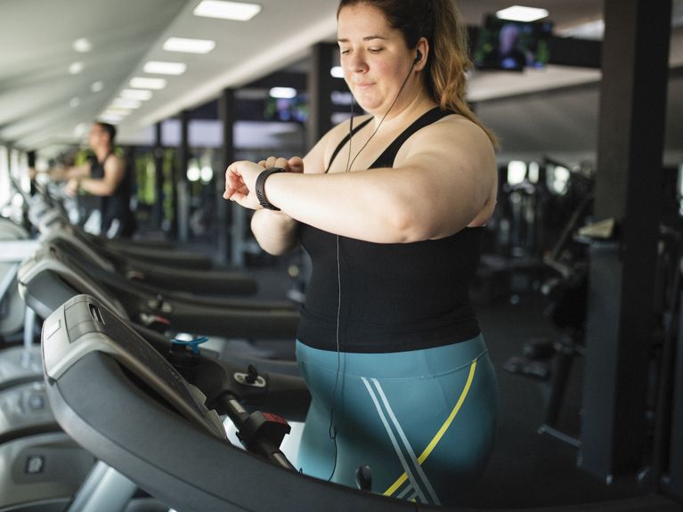 A white woman in teal spandex pants and a black tank on a treadmill