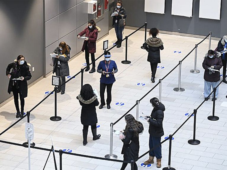 People wearing masks stand socially distanced in a line that wraps around the room.