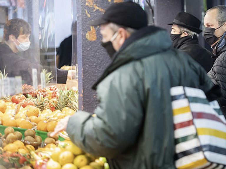 Man with a mask on stands in front of a fruit stand.