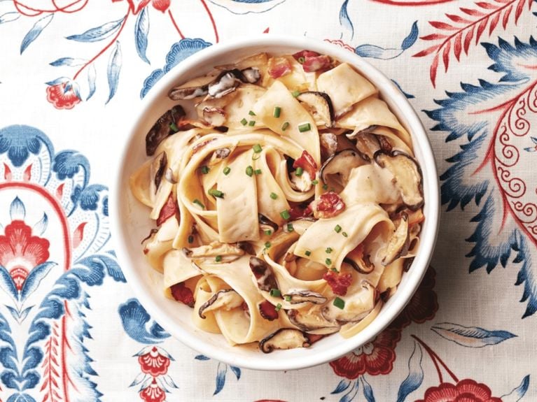 Bacon and mushroom pappardelle in a bowl on a red and white patterned background