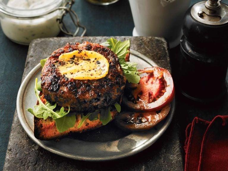 black bean burger with tomato, lettuce, sauce on a toasted bun on a plate