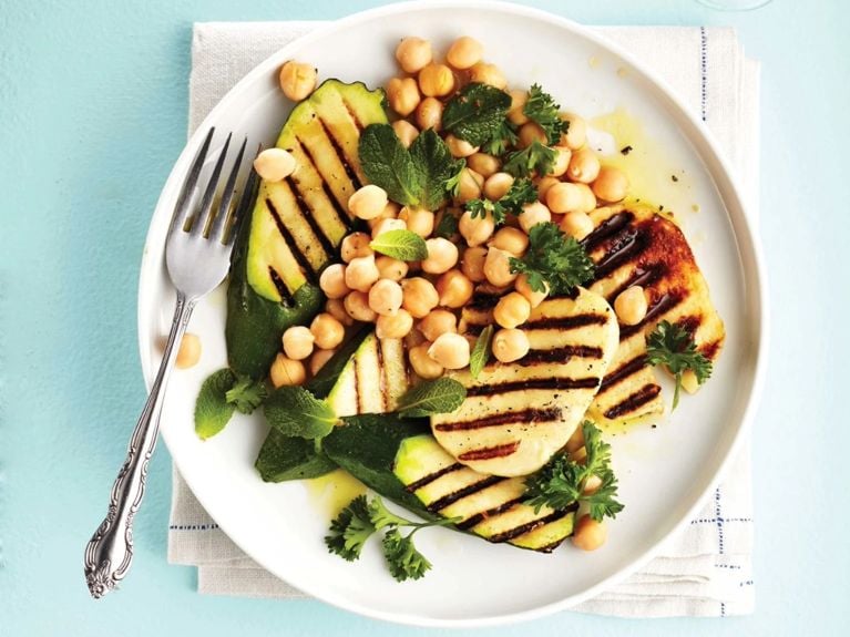 Grilled halloumi and zucchini salad with chickpeas, fresh mint, parsley and lemon on a white plate