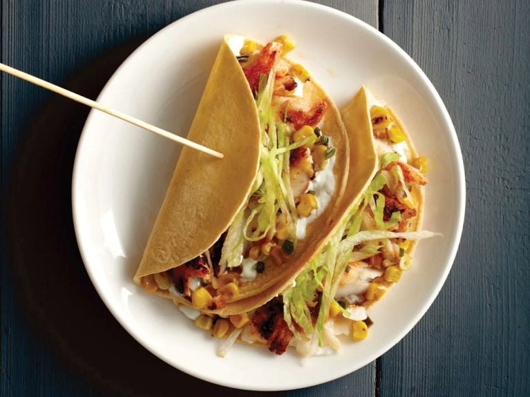 fish tacos in corn tortillas stuffed with veggies on a white plate