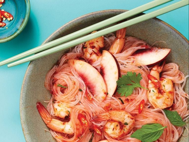 Cold Noodles With Shrimp And Peaches in a bowl topped with chopped cilantro and basil with two green chopsticks resting on the bowl