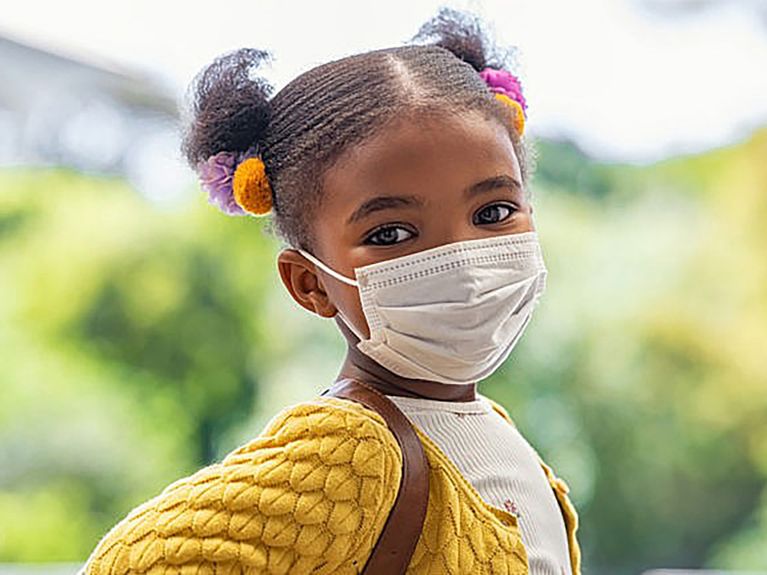 Child stands and looks at camera wearing a mask