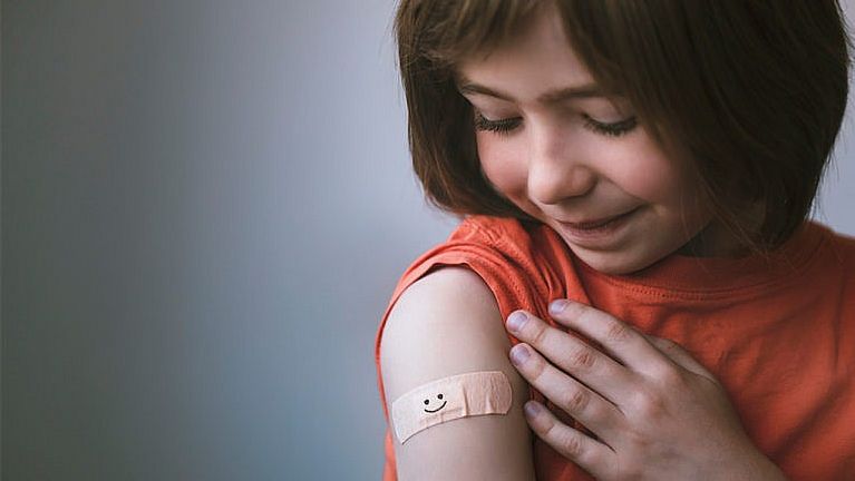 A young girl rolls up her sleeve to look at a band aid on her bicep