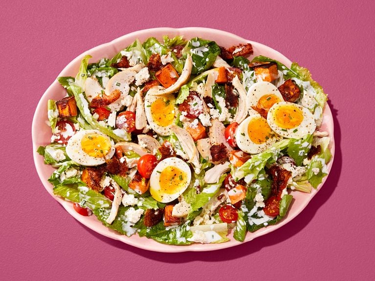 Cobb salad with sliced soft-boiled eggs, tomatoes and chicken in a pink bowl on a pink table.