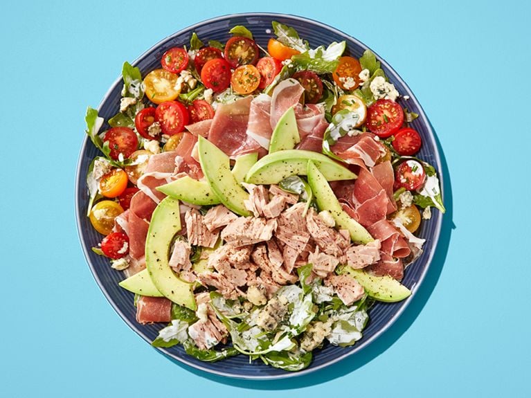 A salad with avocado, tuna, tomatoes on a blue plate on a blue table.