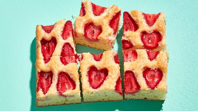 A section of pale yellow snacking cake with inlaid strawberries sliced into six pieces on a turquoise table