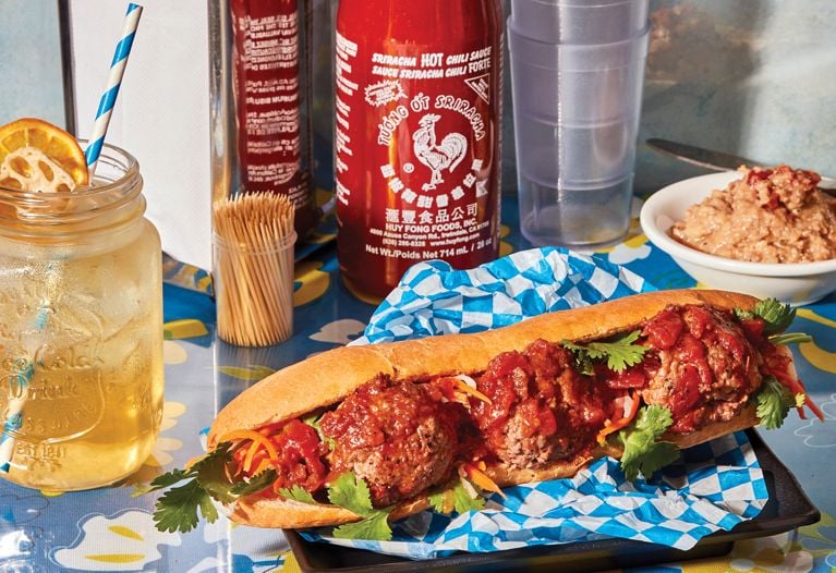 Image of a banh mi with various condiments surrounding it against a blue tablecloth background