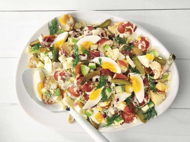 nordic potato salad with hard boiled eggs, pickles, red onions and dill on a white bowl