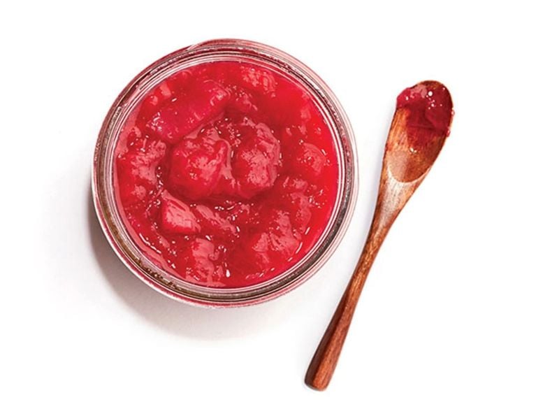 A jar of strawberry jam with a wooden spoon beside it.