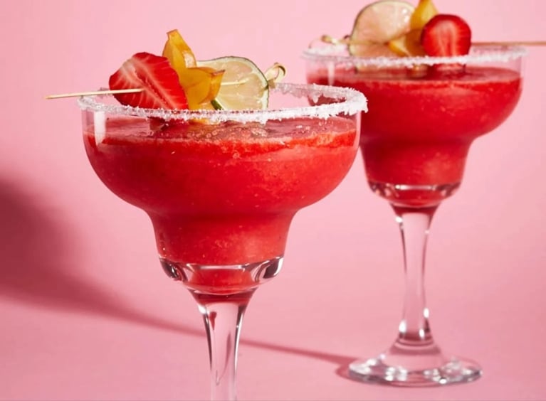 Strawberry margaritas in glasses with a fruit garnish across the top.