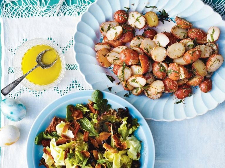 A platter of baby red potato salad on a table next to a green salad and a bowl of vinaigrette