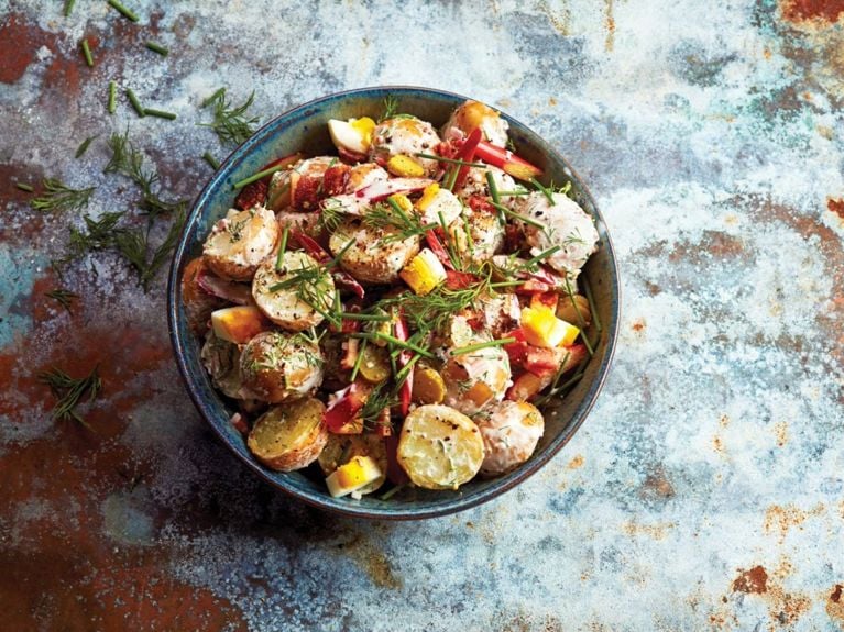 A bowl of creamy rhubarb potato salad, topped with fresh dill; creamy rhubarb potato salad recipe