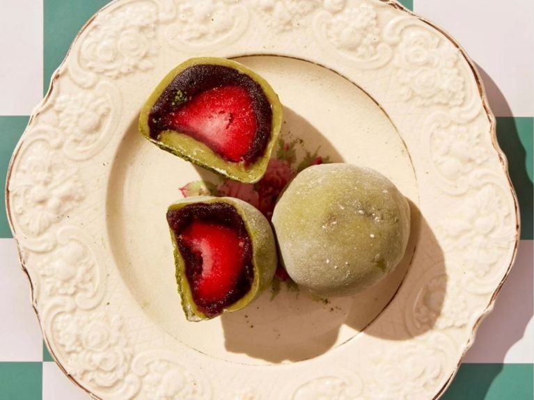 Top view of one whole and two half pieces of Matcha Mochi Strawberry Daifuku served on a plate.