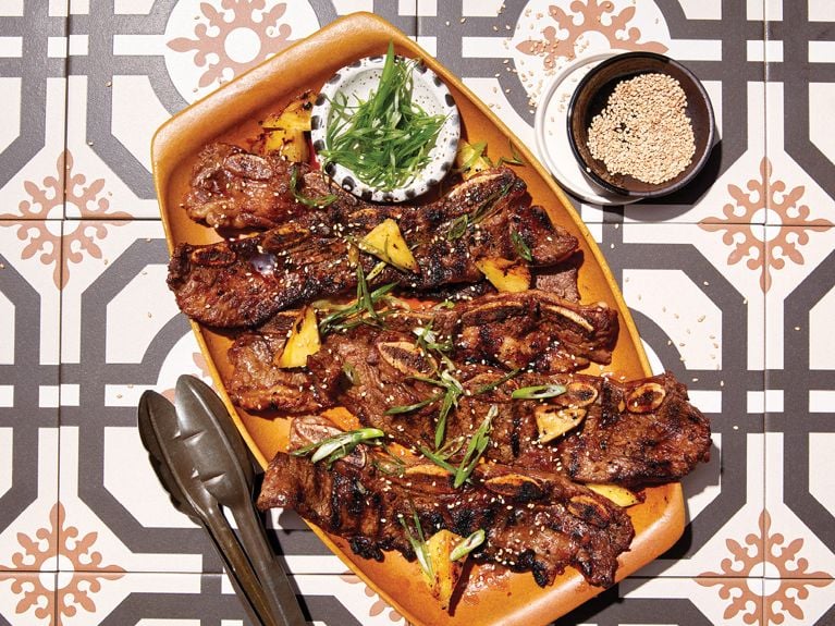 A plate of pineapple-soy-marinated beef short ribs served with sesame seeds and sliced green onions