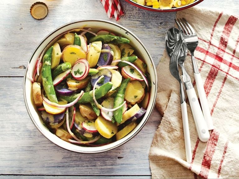 A bowl of parsley salad with parsley vinaigrette with red onion slices; radishes; green beans on a picnic table