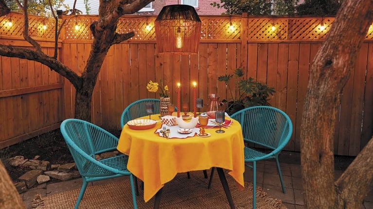 A table set outdoors in a backyard with a solar-powered outdoor pendant light hanging above from a tree.