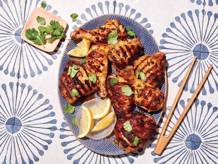 A plate of spiced yogurt-marinated chicken served with lemon slices and cilantro