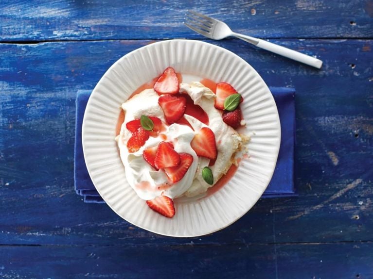 Fresh basil and strawberry meringues on a white plate on a blue table