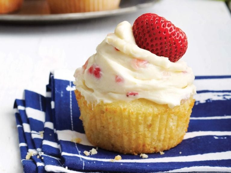 Strawberry and lemon cream cheese cupcakes topped with a fresh strawberry on a blue and white napkin