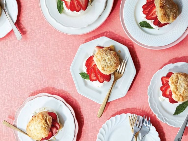 Strawberry shortcake with vanilla cream—cake topped with vanilla cream and sliced strawberries and fresh mint topped with more cake on a white