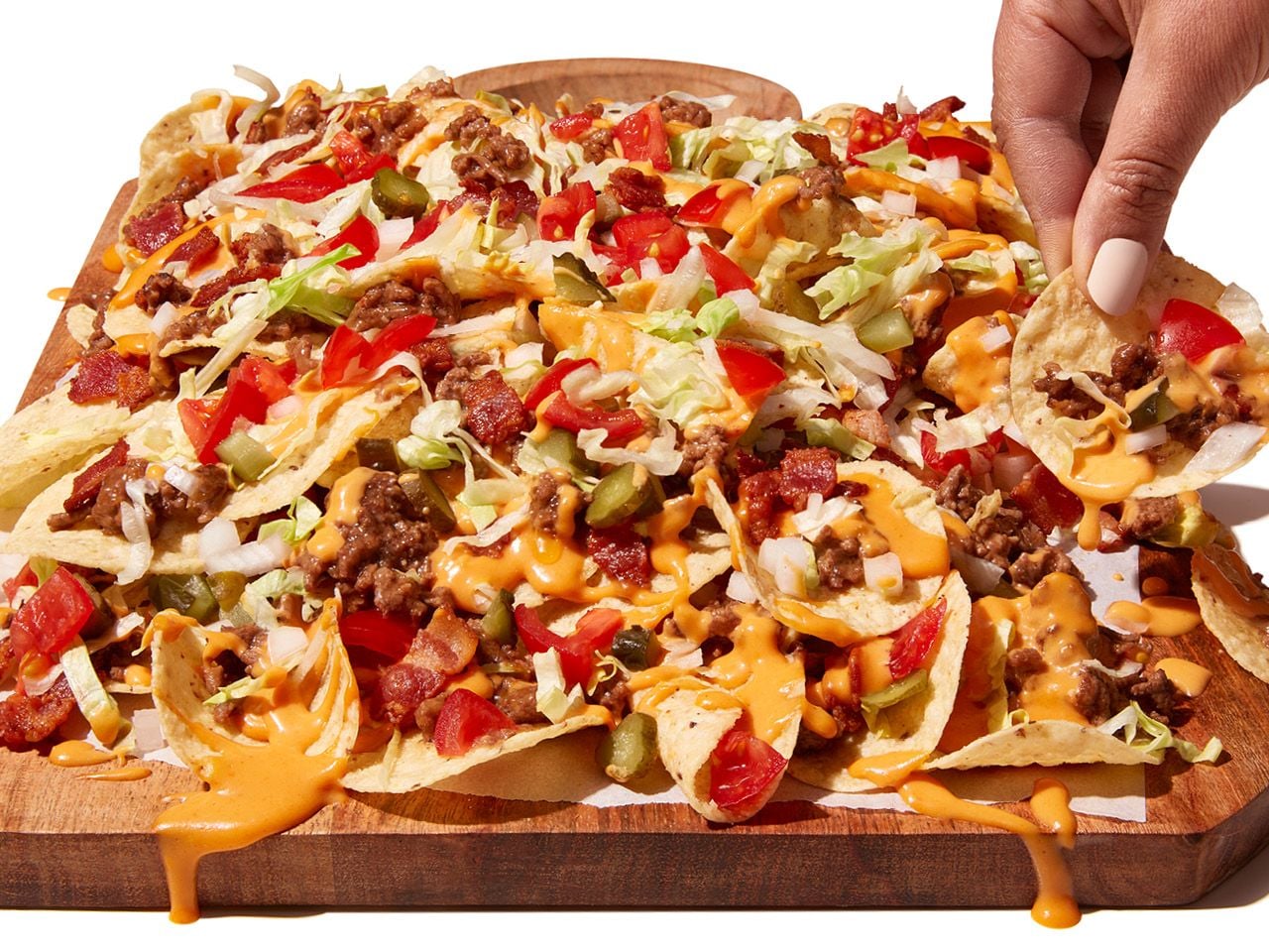 A person picking up a tortilla chip from a tray of Hamburguesa con Queso Nachos