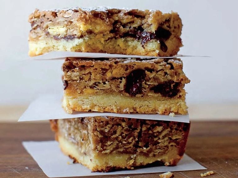  3 Smitten Kitchen Bake Sale Winning Gooey Oat Bars stacked between a white napkin/thin paper for an article about 17 Of Our Favourite Dessert Square Recipes To Make Now