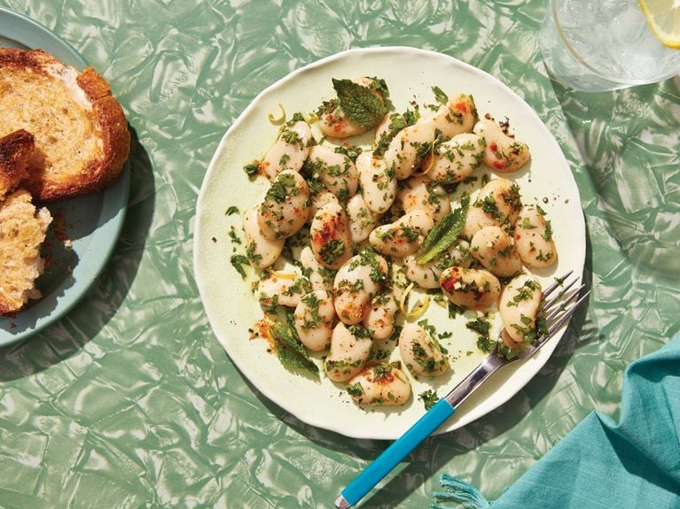 A plate of herb and garlic butter bean salad topped with chopped mint and parsley leaves.