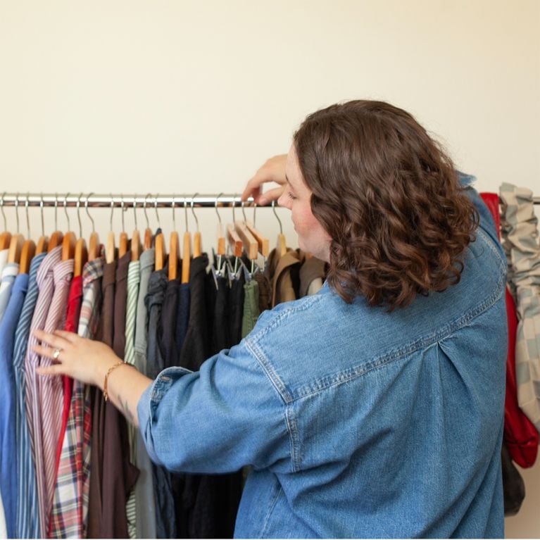 Stylist Alberta Rose pictured in her room skimming through shirts and bottoms on a clothing rack.
